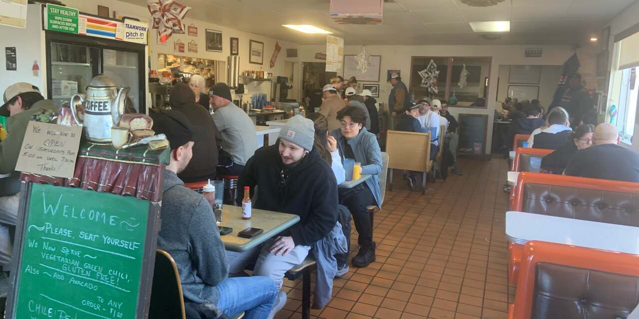 The packed dining room at Butcher Block Cafe: red vinyl booths, the counter, and regulars over breakfast.
